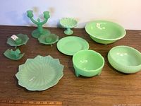 Full view of the jadeite glass items displayed on wooden surface including candlestick holders, plates, and bowls.