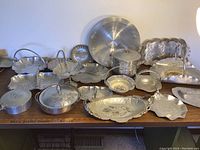 Full overview of all 18 pressed aluminum serving pieces showing variety in shape and size including trays, bowls, baskets, and covered dishes