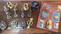 Photo showing all brass door knockers arranged on wooden surface with two brass candlesticks and an antique brass and copper book.