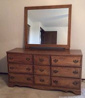 Front view of dresser with attached mirror showing nine drawers and decorative handles.