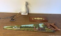 Overview of four items on wood surface: painted saw, ceramic duck head, wood floral plaque, plow figurine
