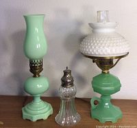 Front view of two jadeite glass lamps and clear glass shaker on table