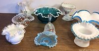 Nine glass items including five milk glass pieces with ruffled edges and painted designs, one teal colored glass bowl with white ruffled edge, a hand painted bell, a basket with strawberry motif, and a turquoise popcorn glass shallow saucer.