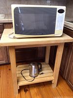 Front angle of Sharp microwave oven and electric kettle sitting on wooden kitchen island in kitchen area.