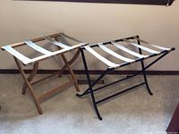 View of two folding luggage stands side by side; one with wood frame and floral straps, the other with black metal frame and white straps.
