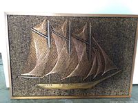 Front view of maritime symmography wire art showing the full sailing ship with detailed wire sails and wooden hull on cork board.