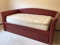 Red upholstered day bed against wall with white tufted twin mattress and pullout trundle underneath
