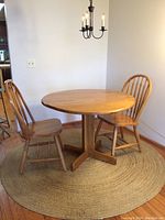 Maple wood round table with two wooden chairs and round woven rug underneath in a corner.