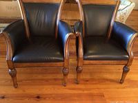 Front view of two black faux leather armchairs with wooden frames and carved front legs.