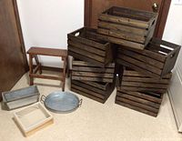 Photo showing seven dark stained wooden crates stacked, small wooden stool, and metal and wood organizers on the floor.