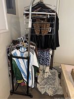 Metal adjustable clothing rack holding several men's and women's clothing items including shirts, jackets, and dresses. Clothes are size medium (men) and size small (women).