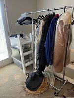 Clothing rack with men's and women's jackets and shirts plus hats on the floor, showing outerwear including genuine shearling jacket.