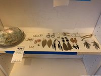 Shelf with an array of earrings including hoop, leaf-shaped, chain tassel and dangle styles in silver, gold, black, and green tones.