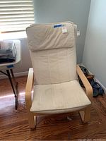 Front view of the IKEA wooden frame chair with light beige upholstered cushion showing stitching and curved wooden armrests.