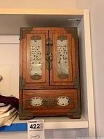 Front view of vintage wooden jewelry box with decorative metal inlays, two doors on top, and a drawer below.