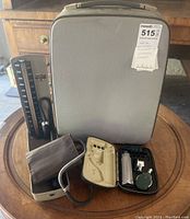 Photo showing gray hard carrying case, sphygmomanometer with cuff and gauge, and small zippered case with diagnostic tools arranged on round table.