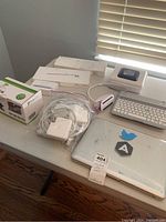 Photo showing MacBook Pro laptop with stickers, Apple accessory boxes, label maker, keyboard, and cables on a table.