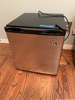 Front view of mini fridge showing stainless steel door and black top with power cord on hardwood floor.