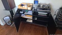 Wide view of black desk cabinet with various office supplies arranged on top and inside drawers.