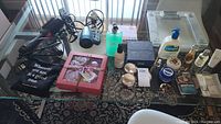 Photo showing all items on glass table including hair dryer, hot air brush, skincare bottles, 23andMe kit, Le Labo fragrance box, pink boxed bath fizz set, bathroom scale, and other personal care items.