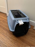 Front view of the gray and black plastic pet carrier with black metal front door and ventilation openings on the sides.