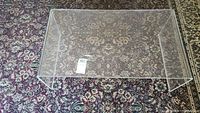 Top view of the clear plexiglass table placed on a patterned carpet, showing the rectangular shape and transparency of the table.