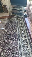 Photo showing part of the Persian-style rug next to a glass table and TV stand, displaying the detailed floral pattern in dark red and cream colors.