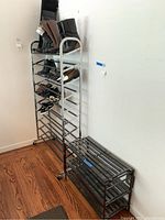 Tall chrome-finished metal shoe rack holding multiple shoes, positioned next to a shorter black metal shoe rack on hardwood floor.
