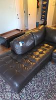 Brown leather sectional sofa with tufted cushions positioned on patterned carpet in living room.