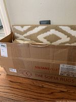 Box containing white and golden carpet stair treads with geometric diamond pattern.