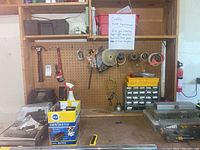 Workbench and pegboard with various tools, spray bottles, parts organizer, and boxes including Dentastix.