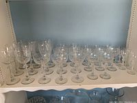 Photo showing multiple clear vintage stemmed glasses with etched patterns arranged on shelf