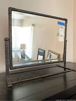 Front view of the full vintage metal frame mirror sitting on a table, showing its rectangular shape and reflective beveled glass.