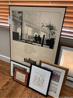 Five framed wall art pieces on floor near window. One large Manhattan movie poster leaning against wall, four smaller framed prints in front.