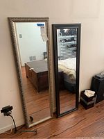 Two floor mirrors side by side showing one with ornate silver frame and the other with plain black frame