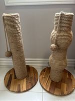 Two cat scratchers side by side showing different shapes with hanging ball toys on wooden bases.