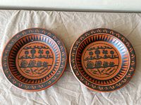 Two ceramic bowls with black and terracotta Scottie Wilson folk art designs including animals and geometric patterns.