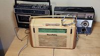 Three old transistor radios on a wooden surface, showing front and top views.