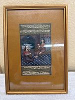 Front view of framed Arabic miniature painting depicting two figures with calligraphy above and below the image.