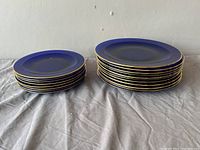 Two stacks of blue cobalt glass plates against a plain background; the stack on left is smaller (side plates), the larger stack on the right (dinner plates).
