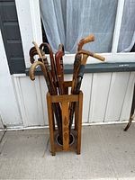 Front view of wooden cane stand filled with multiple assorted wooden canes of various handle styles and heights.