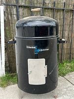 Full view of the black Char-Broil H2O Smoker showing the vertical cylindrical body, metal legs, side wooden handles, and front access door with latch.