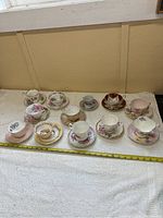 All 10 assorted porcelain cups and saucers displayed on fabric with measuring tape showing size.