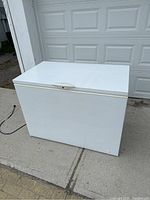 Frigidaire white chest freezer with top lid closed, viewed from front side showing general condition and size.