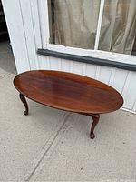 Full view of the oval mahogany coffee table on four cabriole Queen Anne legs outside a building.