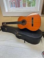 Left handed Capri acoustic guitar resting on black hard shell case near window.