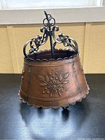 Full view of copper-toned metal chandelier with floral embossing and wrought iron scrollwork on top.