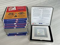 Stack of collectible tins with one opened showing a hologram stamp inside, certificate and informational card on the lid.