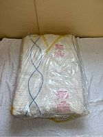 Front view of wrapped vintage chenille bedspread showing multicolored diamond pattern lines in blue, yellow, and green on a cream background.