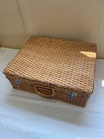 Closed wicker picnic basket with one front handle and metal latches.